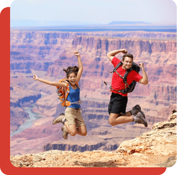 Two hikers standing in front of the Grand Canyon and jumping for joy.