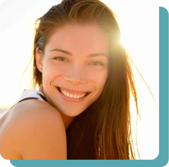 Close up of a young woman’s smiling face with the sun shining in the background.